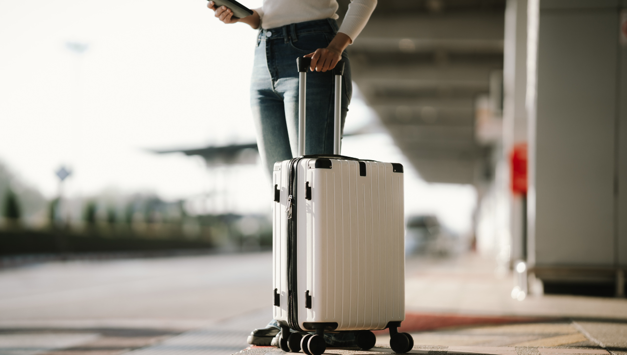 Mulher com mala de viagem num aeroporto, a consultar o telemóvel junto à zona de bagagens